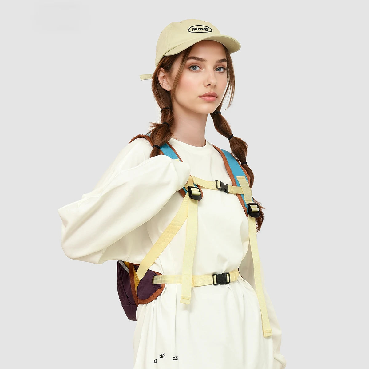 A woman wearing a beige cap and white shirt with a tan backpack is shown in a studio setting.