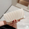 A hand holds a light beige luxury chain shoulder clutch bag with pleated texture against a bright background.