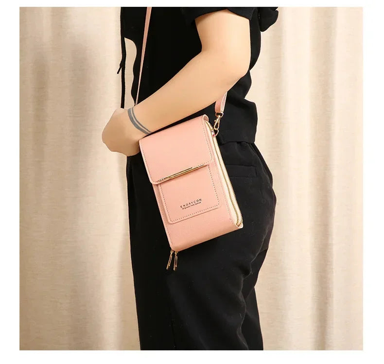 A woman holds a light pink leather touchscreen crossbody shoulder bag against a neutral background.