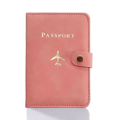 A pink leather passport holder with a gold embossed word and a small gold airplane charm.
