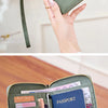 A black leather passport wallet with a gold clasp and wrist strap is shown being held by a person.