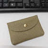 A tan genuine leather card holder with a stitched texture and a round brass stud, placed on a white surface.