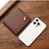 A brown leather wallet with a money clip resting on a wooden surface next to a white smartphone.
