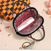 A black portable earbud case with a pink velvet lining is shown next to an orange checkered box and a gold keychain charm.