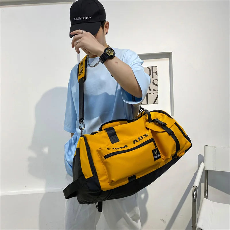 A person wearing a black cap and light blue shirt holds a yellow tactical backpack.