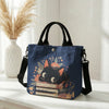 Dunkelblaue Tasche mit Blumen-Katzenmuster und schwarzen Riemen, auf weißem Untergrund.