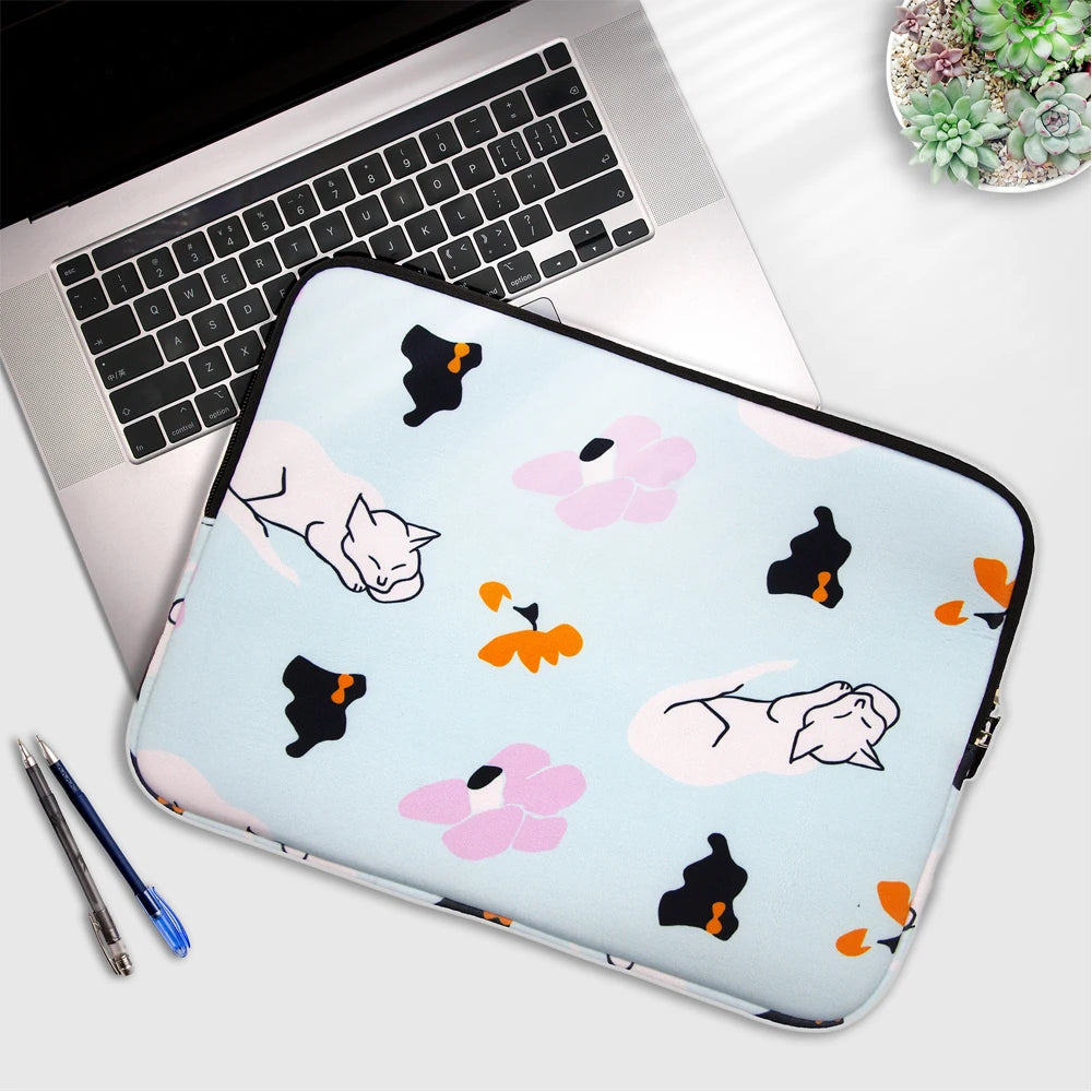 A light blue laptop sleeve featuring cute black and pink floral cat illustrations placed on a silver laptop.