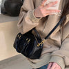 A person holds a black vintage PU leather shoulder bag against a beige hoodie.