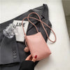 Un bolso cruz de cuero rosa con correa beige junto a una tarjeta blanca en un blazer gris.