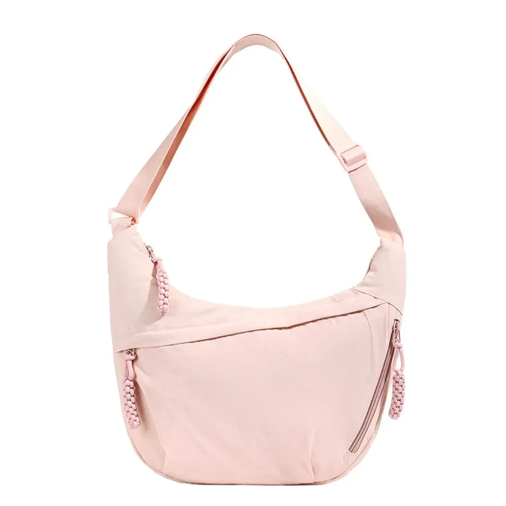 A light pink canvas crossbody bag with a thin strap shown against a white background.