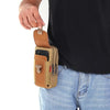 A hand is holding a tan tactical belt pouch designed to hold a mobile phone and keys.