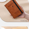 A brown leather passport wallet with a black sleeve and a gold-colored thread detail is shown being held by a hand.