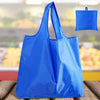 A bright blue reusable foldable grocery tote bag is shown against a blurred background of groceries.