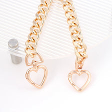 Gold heart-shaped metal purse chain extender displayed on a clear background.