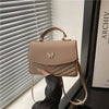 A tan textured shoulder messenger bag is displayed next to a window blind.