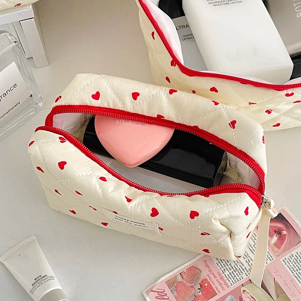 A quilted white makeup bag with red trim and a pink heart-shaped pouch, resting on a light surface.