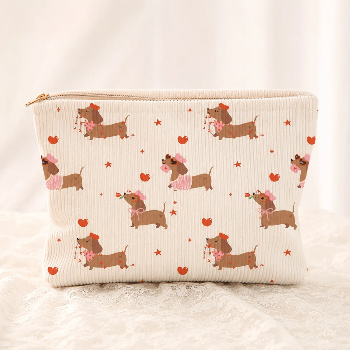 A beige corduroy cosmetic bag with a zipper and a repeating pattern of pink dachshunds and red hearts.