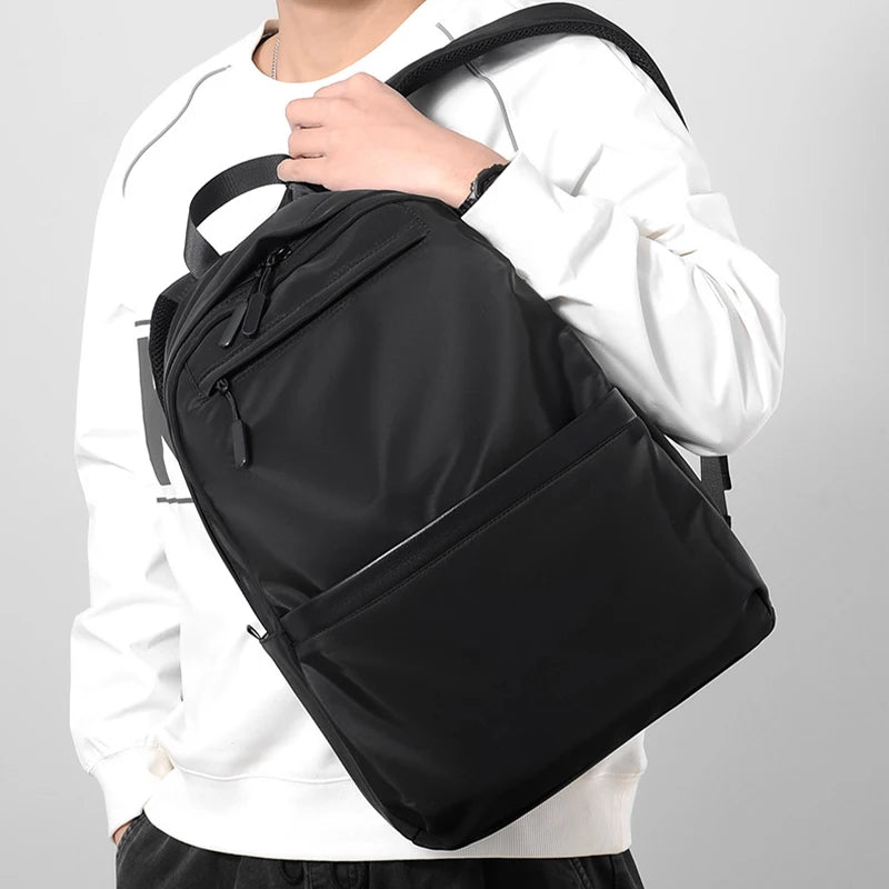 A black ultralight waterproof laptop backpack worn by a person in a white long-sleeved shirt.