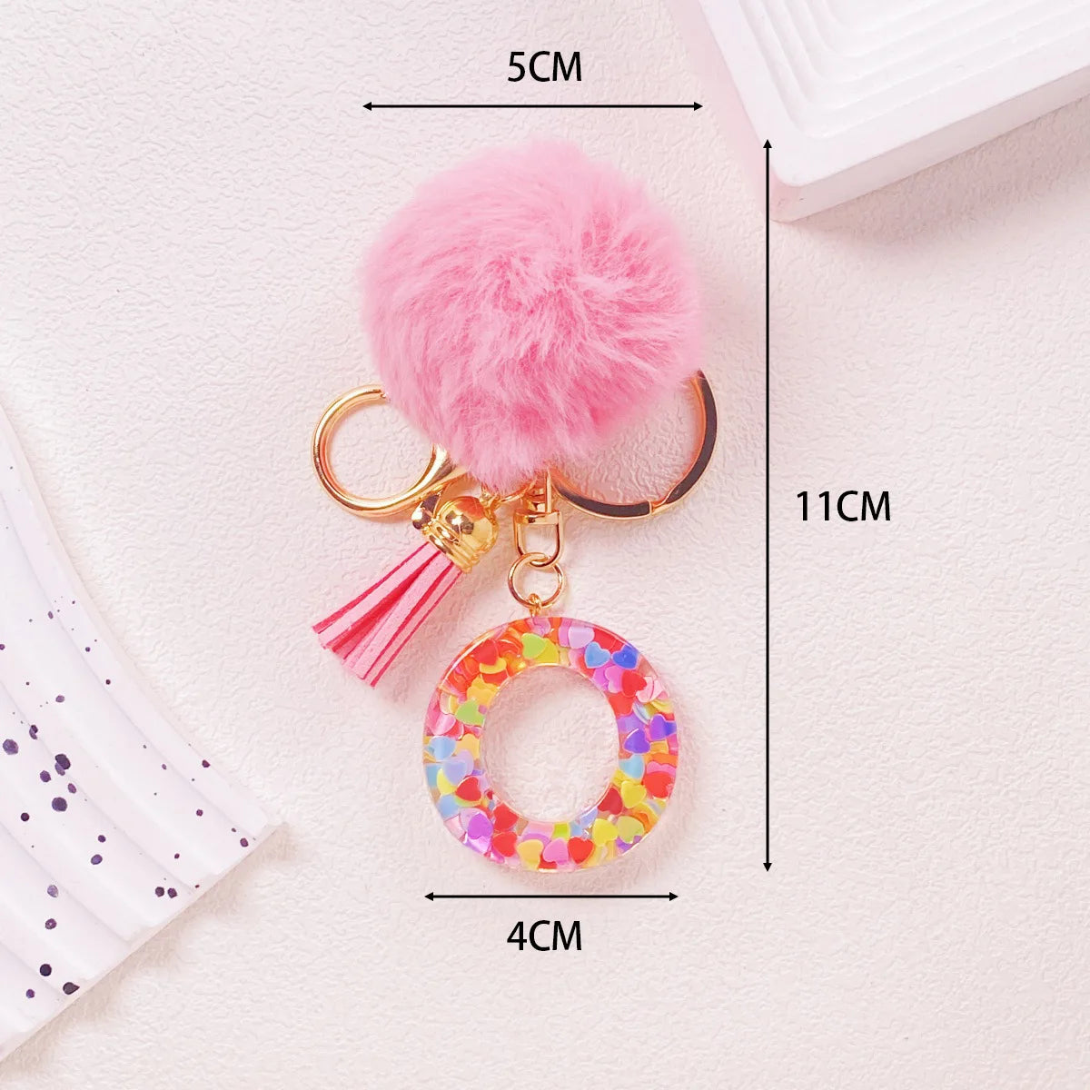 Pink fluffy pom-pom keychain with a shiny resin pendant and alphabet charm
