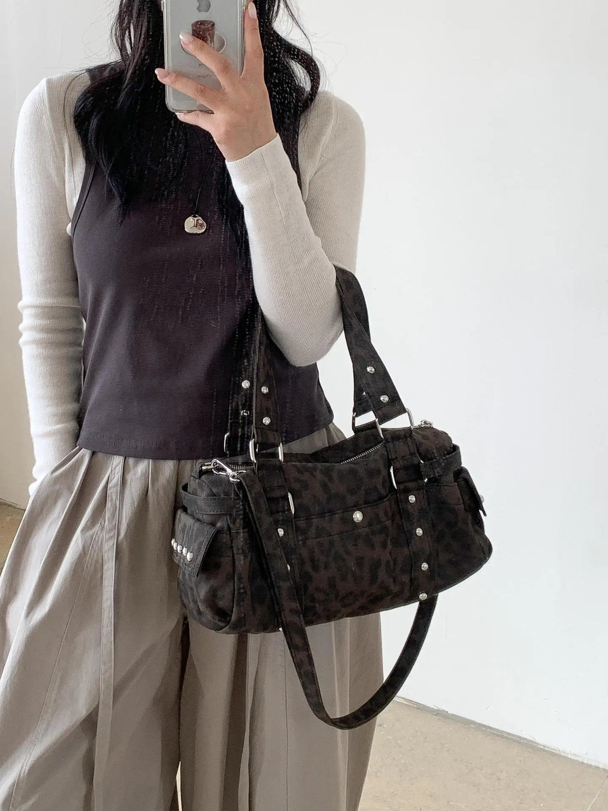 A woman holds a leopard print riveted shoulder bag against a white background.