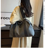 A woman is holding a gray leather Oxford cloth travel tote bag with black straps in a studio setting.