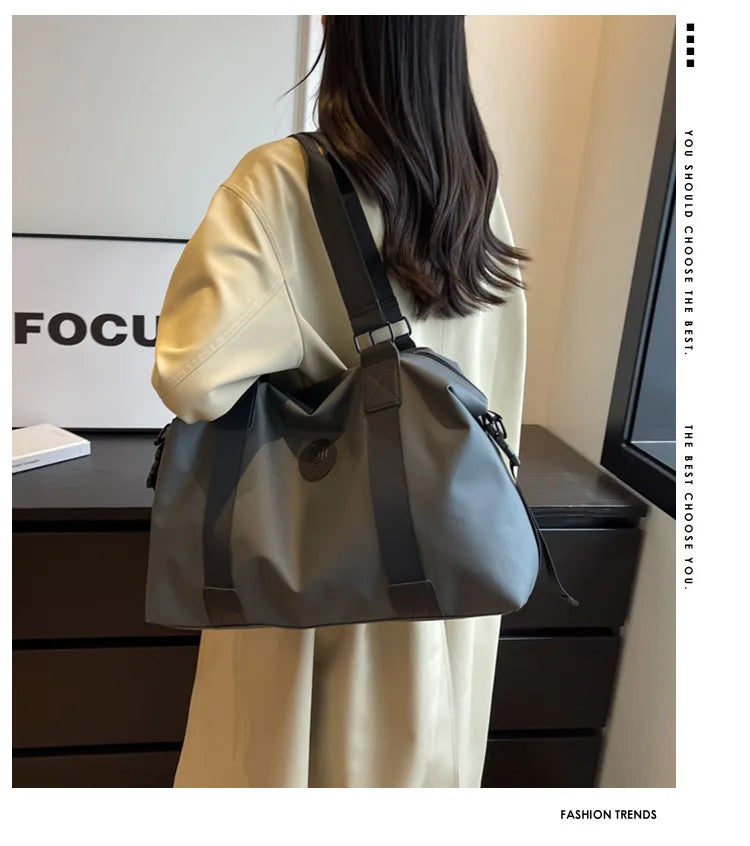 A woman is holding a gray leather Oxford cloth travel tote bag with black straps in a studio setting.