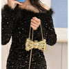 A woman models a gold heart-shaped acrylic evening clutch with a chain strap against a light blue background.