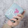 A hand holds a light blue cartoon mini zipper coin purse featuring a pink glitter heart design.