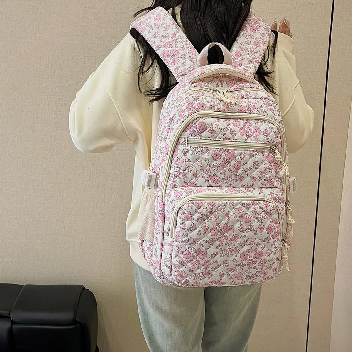A person is wearing a pink floral quilted backpack set on their back.