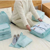 A light blue fabric storage organizer set with various pouches and bins is displayed on a bed.