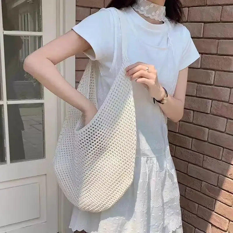 A woman wearing a white dress and holding a white crochet shoulder bag with mesh detailing outside a doorway.