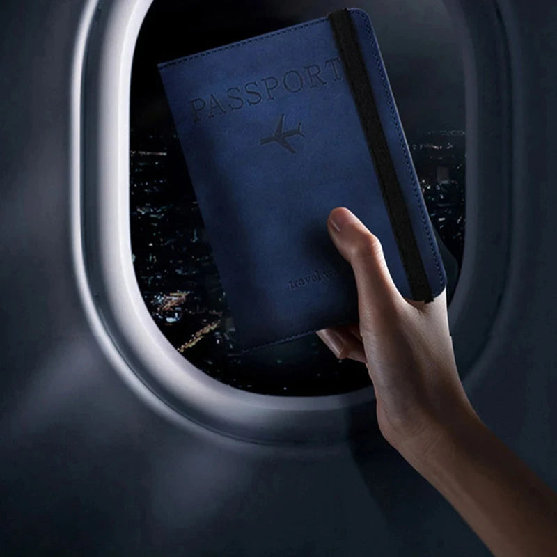 Eine Hand hält eine dunkelblaue Reisepasshülle mit silbernem Flugzeugemblem, betrachtet durch ein Flugzeugfenster.