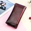A dark brown genuine leather vintage clutch wallet resting on a pink surface next to a photo.