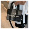 A woman holds a black and gray plaid tote bag with white text on it against a light background.