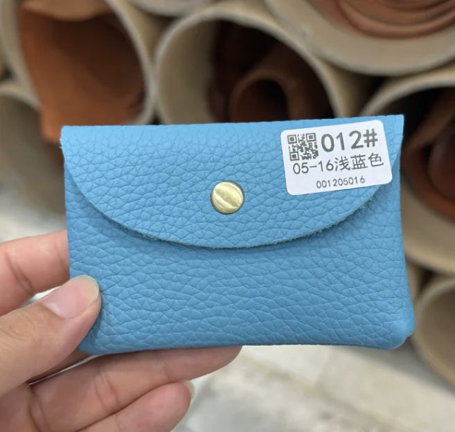 A light blue genuine leather card holder with a gold stud, shown being held by a hand.