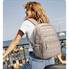 A woman wearing a white shirt and jeans is smiling while carrying a beige quilted casual backpack outdoors by the sea.