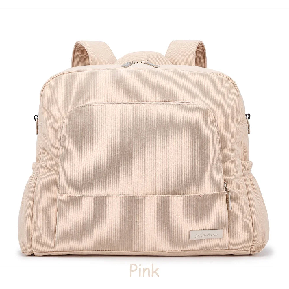 A light pink soft corduroy diaper backpack with padded straps and pockets.