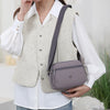 A woman wears a beige vest over a white shirt and carries a gray nylon crossbody bag.