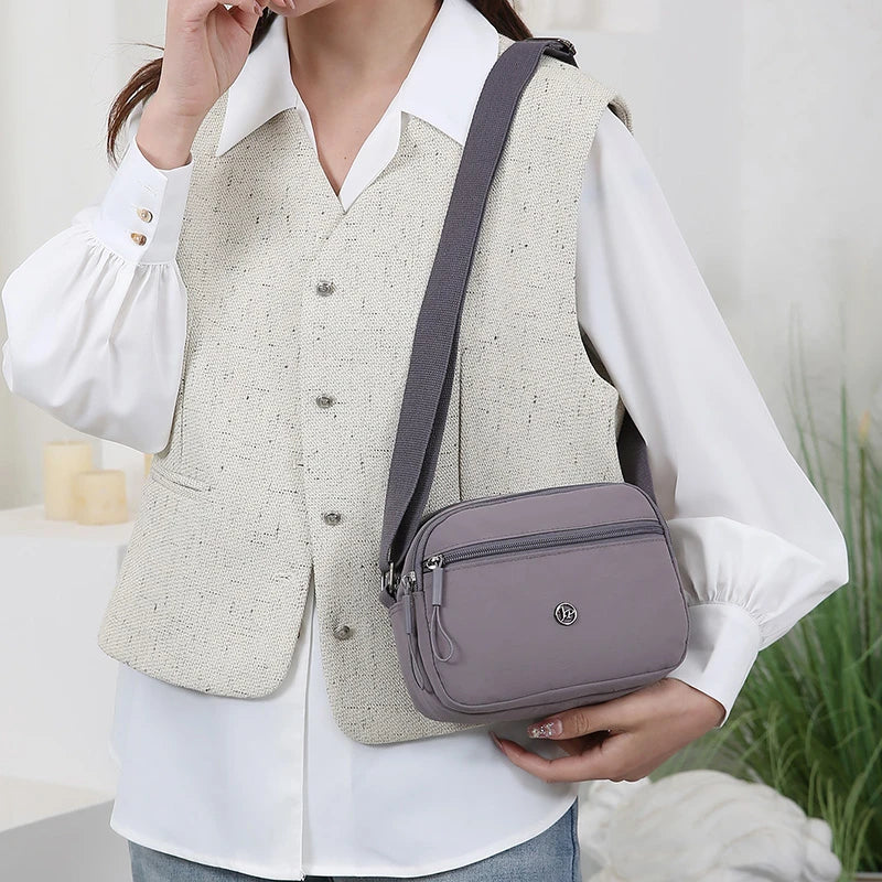 A woman wears a beige vest over a white shirt and carries a gray nylon crossbody bag.