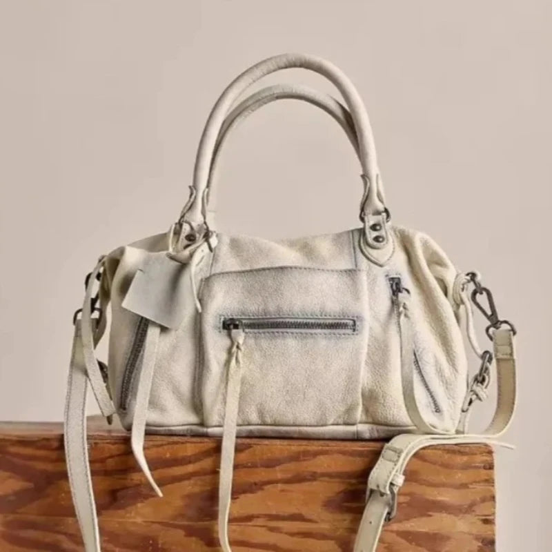 A cream-colored vintage PU leather crossbody tote bag with adjustable straps resting on a wooden surface.