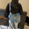 A woman is holding a denim crossbody bag with yellow embroidery against a dark background.