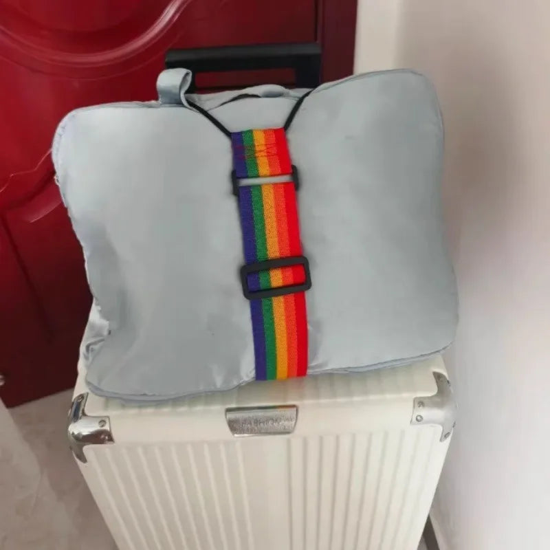 A light blue cushion-like item with a rainbow colored strap is placed on top of a white suitcase.