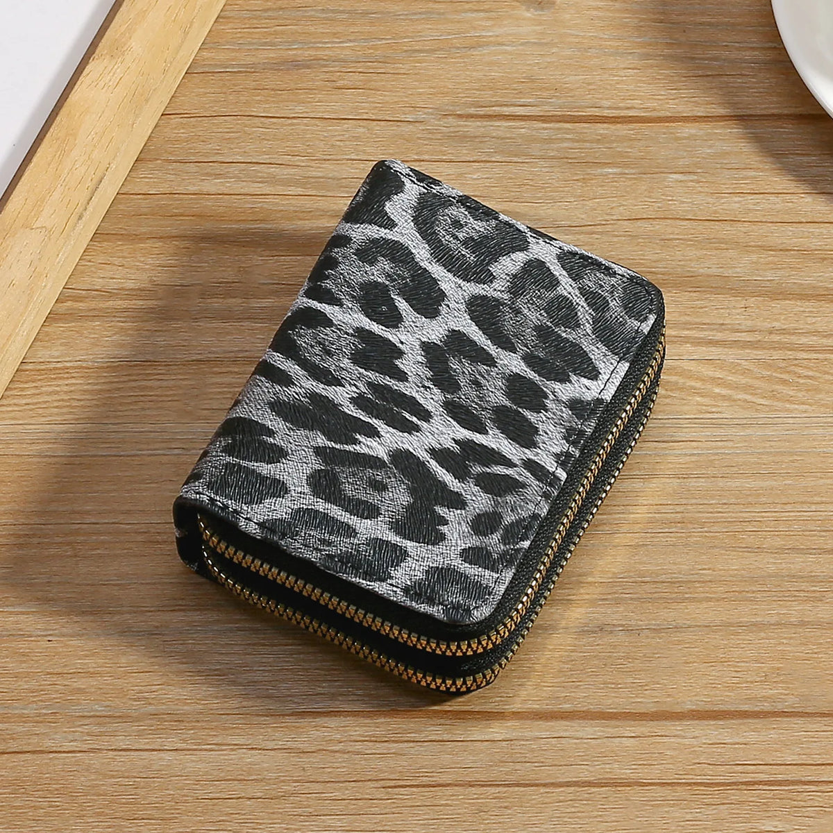 A black and white leopard print double zipper wallet resting on a wooden surface.