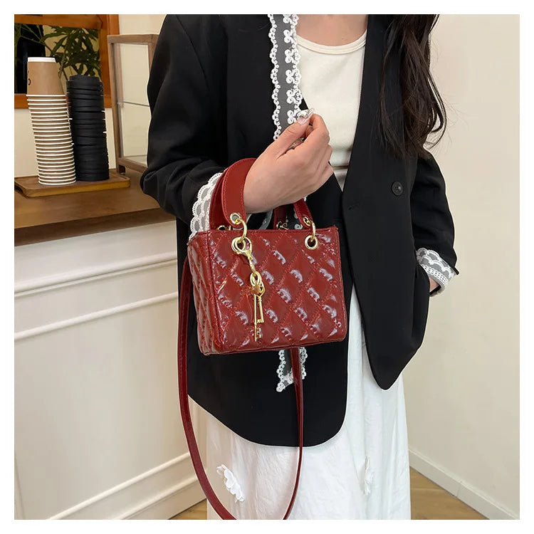 A woman holds a red diamond grid textured crossbody bag with gold hardware against a white top and black blazer.