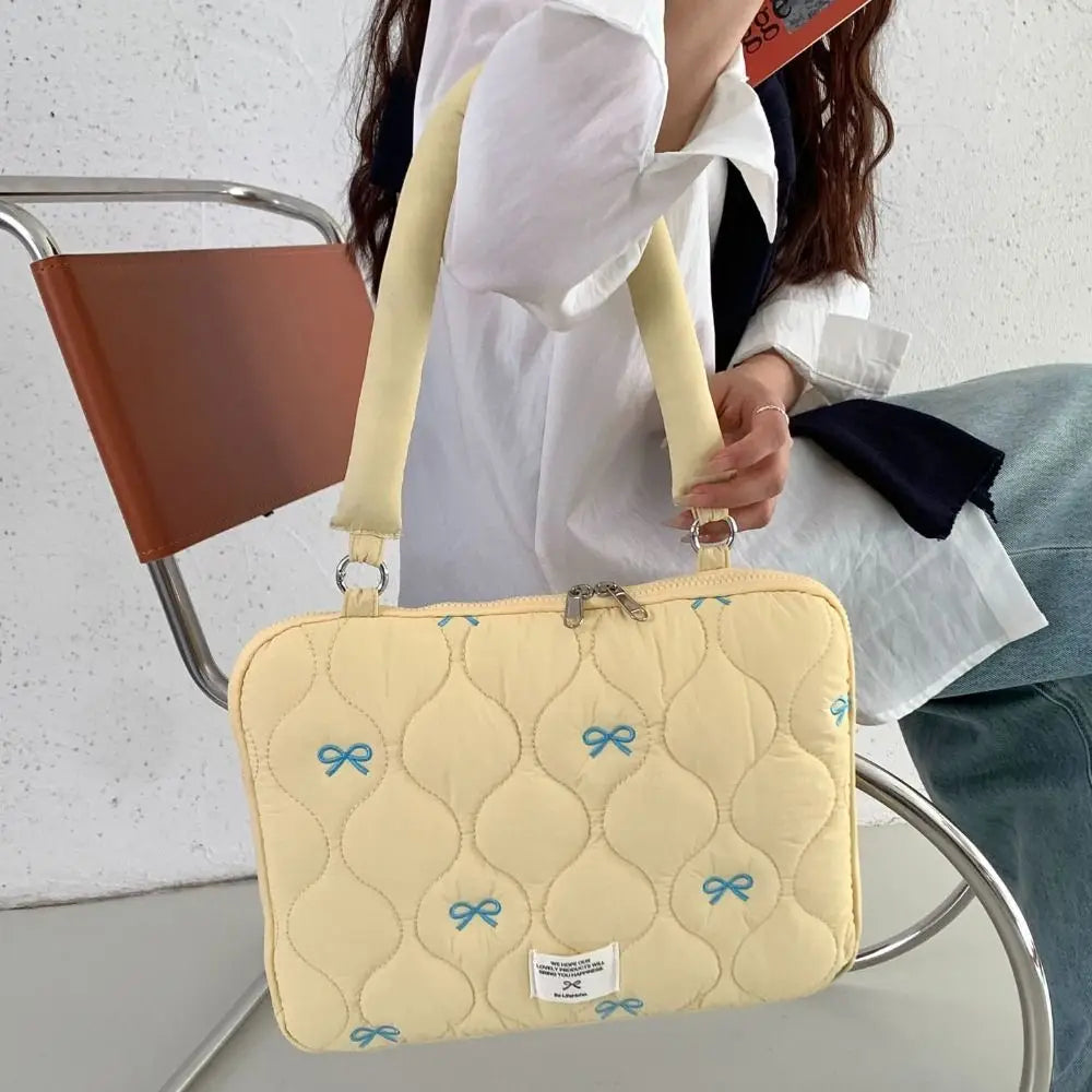 Bolso para portátil acolchado amarillo claro con detalles de lazo azul llevado por una persona.