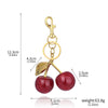 A gold-colored crystal cherry fruit keychain with a hanging loop and a red, glittery cherry sphere.