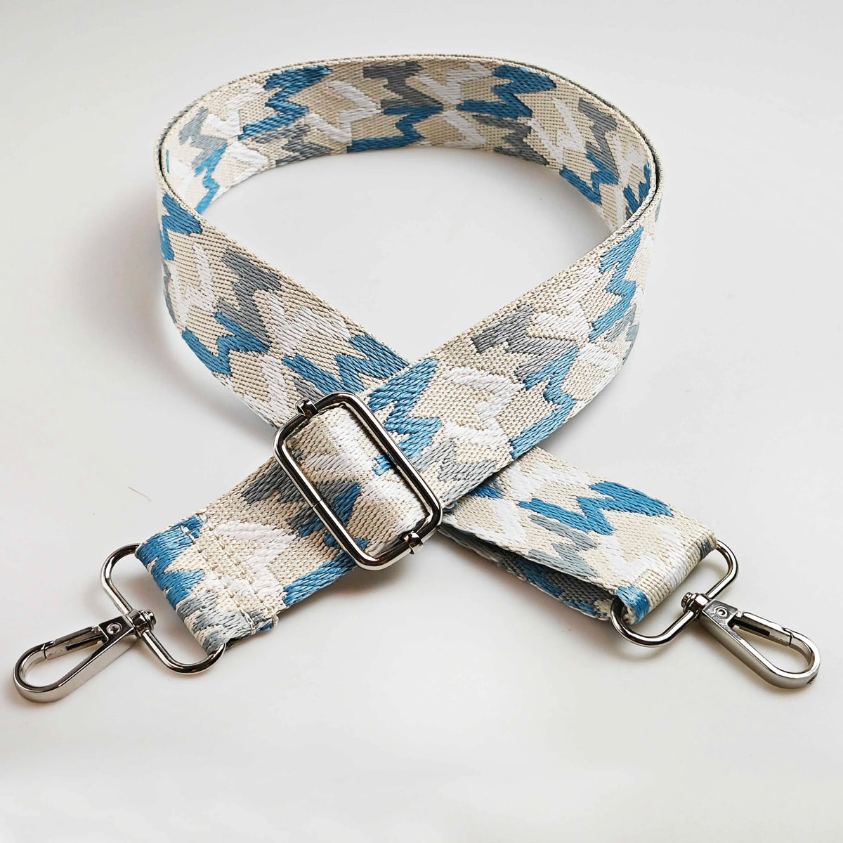 A beige and blue patterned fabric strap with a silver buckle and metal hardware.