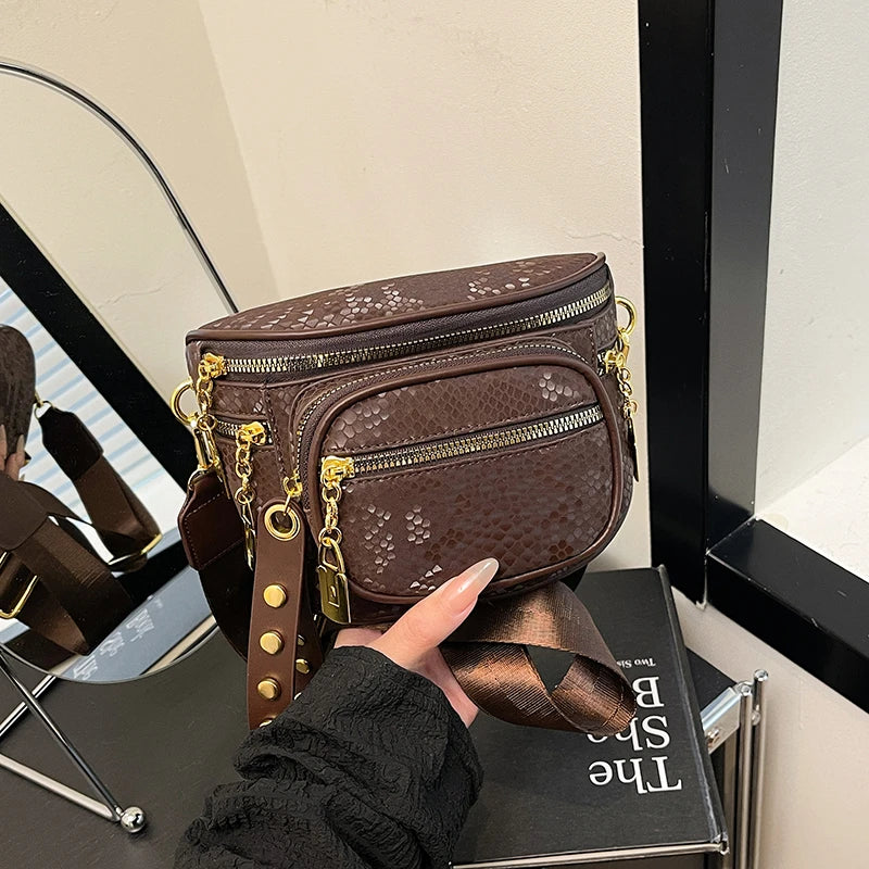 A brown women's riveted waist bag crossbody fanny pack is shown being held by a hand.