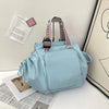 A light blue nylon shoulder bag with a patterned strap is displayed next to some papers.