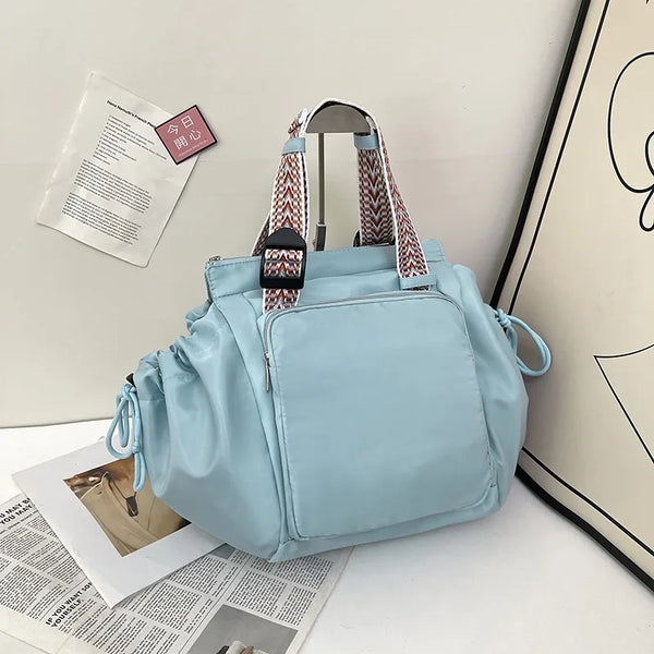 Sac à l'épaule en nylon bleu clair avec une sangle à motifs, exposé à côté de papiers.
